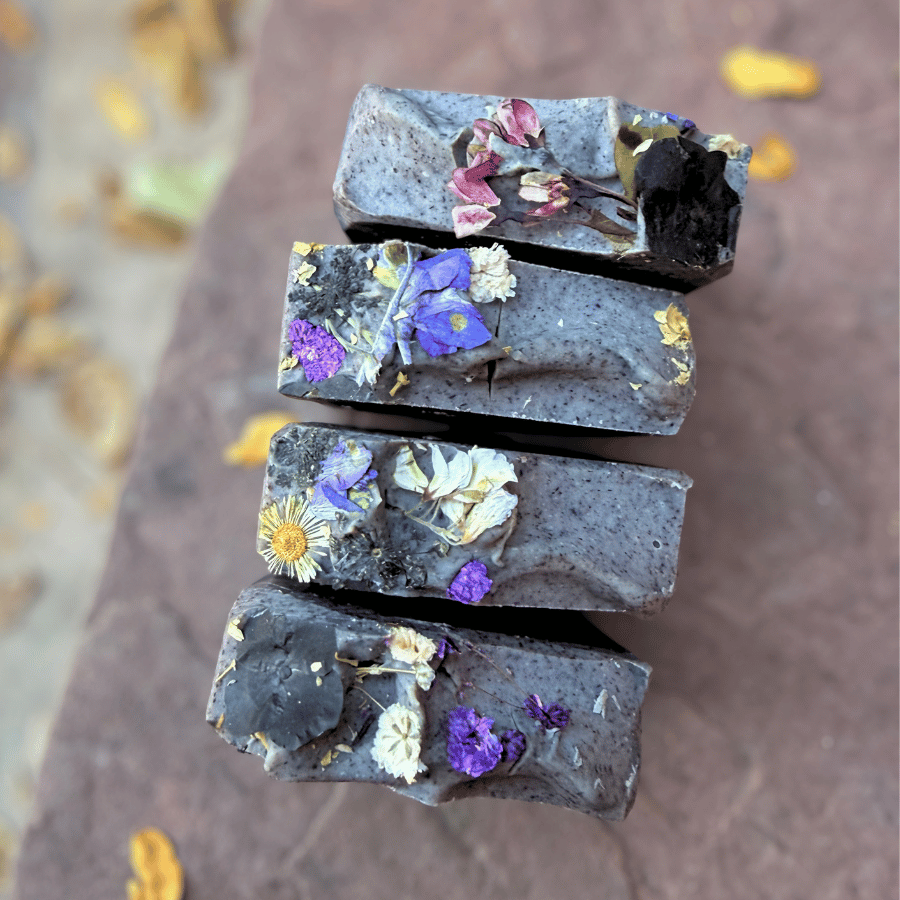 Overhead view of four charcoal tallow soap bars decorated with purple, pink, and white pressed wildflowers.