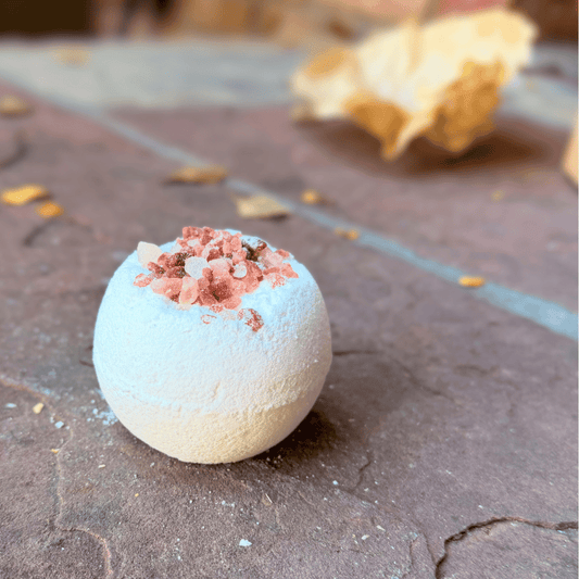 White Magnesium Relaxation Bath Bomb with pink Himalayan salt crystals on top, photographed on a rustic stone surface.