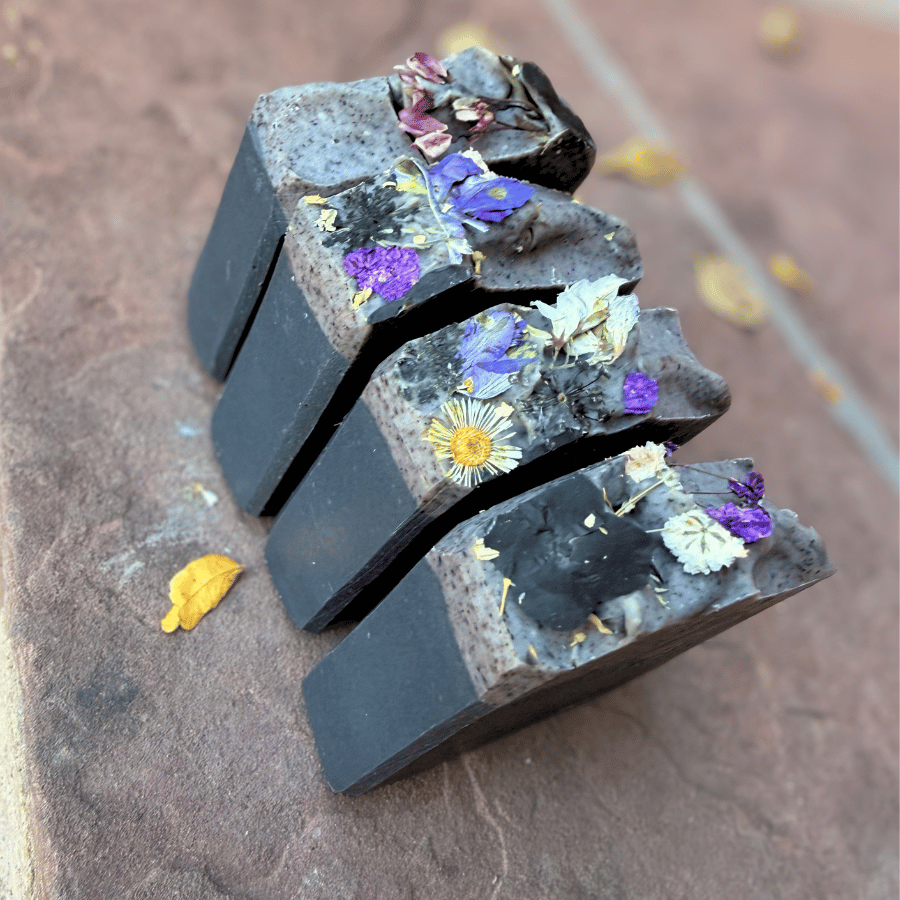 Angled view of handmade Deep Violet charcoal soap bars with dark black bases, smoky gray swirls, and dried botanicals.