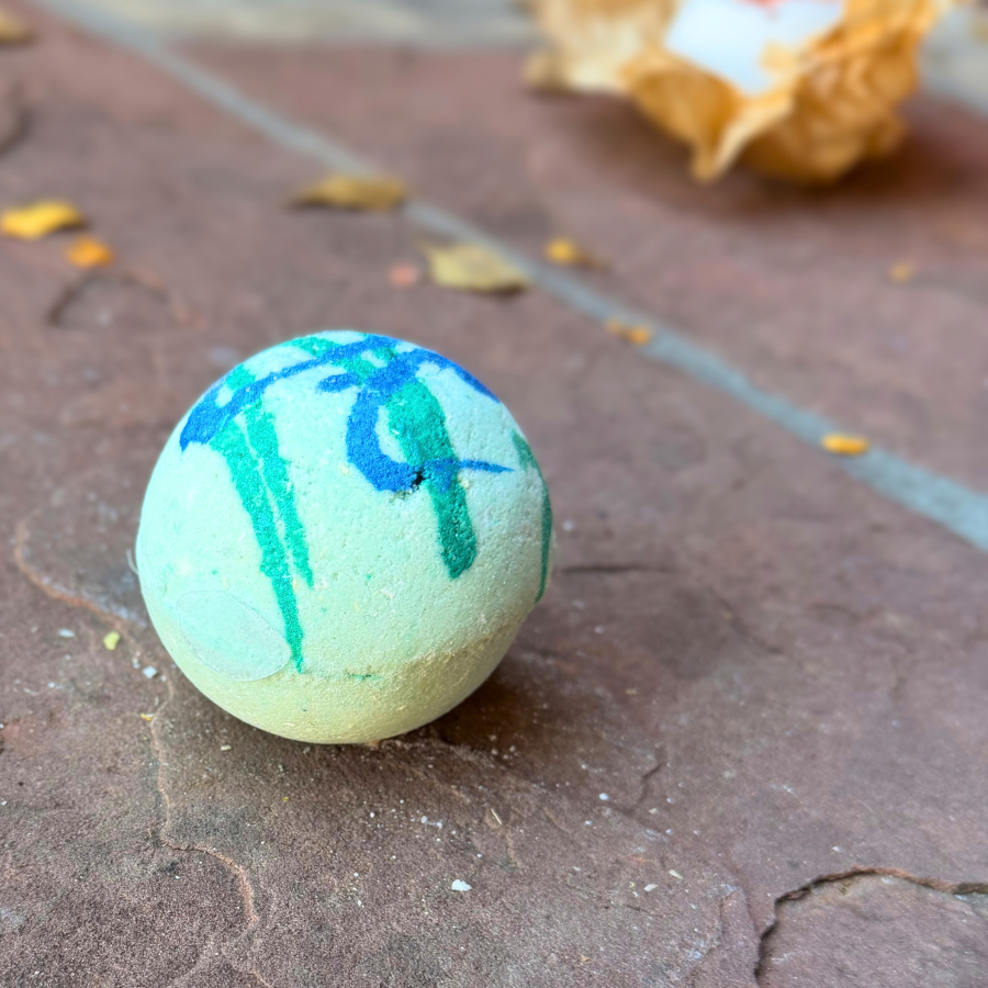 Dinosaur Surprise Bath Bomb with blue and green hand-painted swirls on a pale green surface.