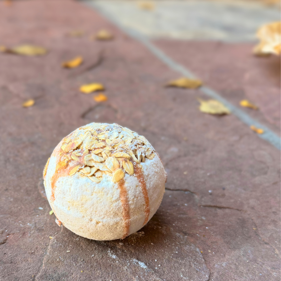 Oatmeal & Honey Bath Bomb with golden drizzle and rolled oat topping on a rustic stone surface.