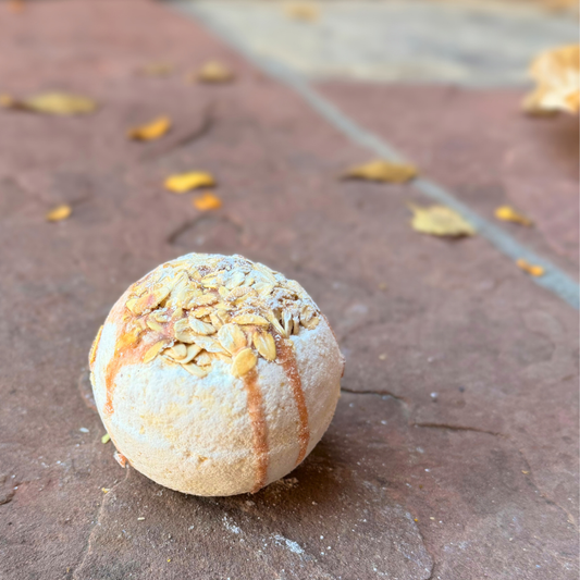 Oatmeal & Honey Bath Bomb with golden drizzle and rolled oat topping on a rustic stone surface.