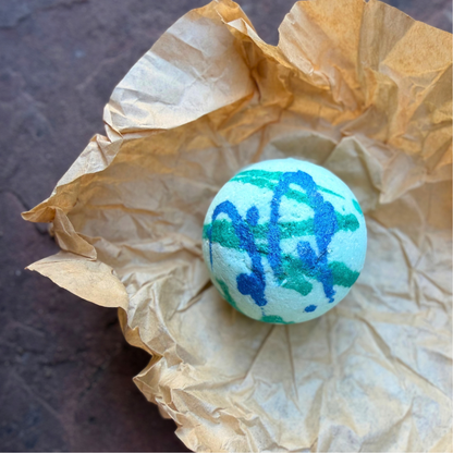 Overhead view of blue and green Dinosaur Surprise Bath Bomb nestled in natural kraft tissue paper.