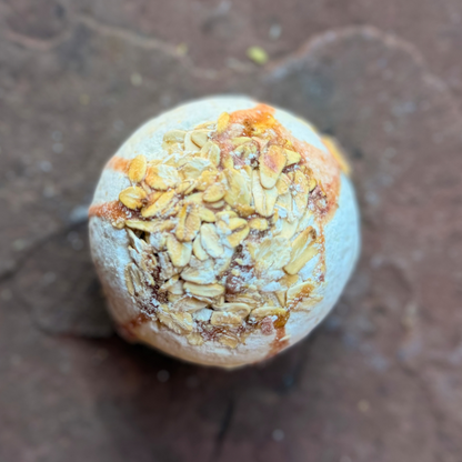 Overhead close-up of Oatmeal & Honey Bath Bomb showing rolled oats and golden hand-painted details.