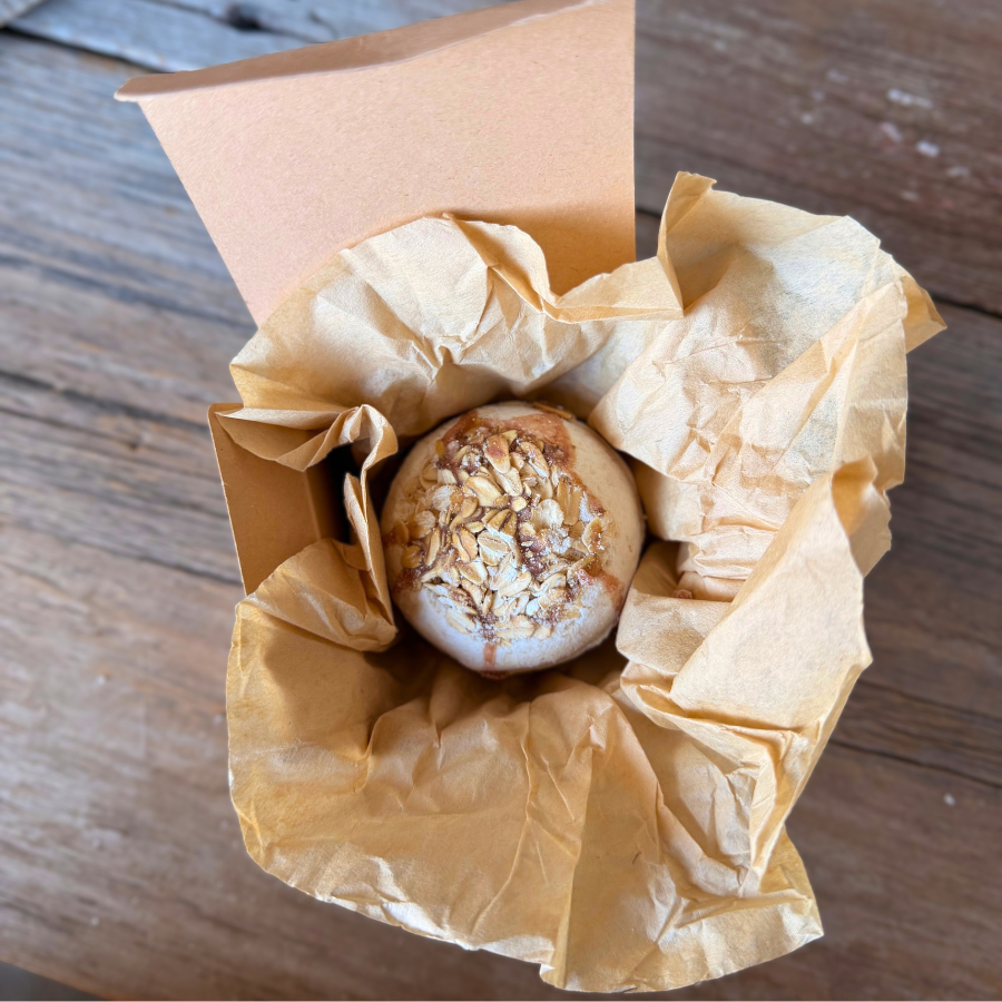 Oatmeal & Honey Bath Bomb nestled in natural kraft tissue paper inside an open gift box.