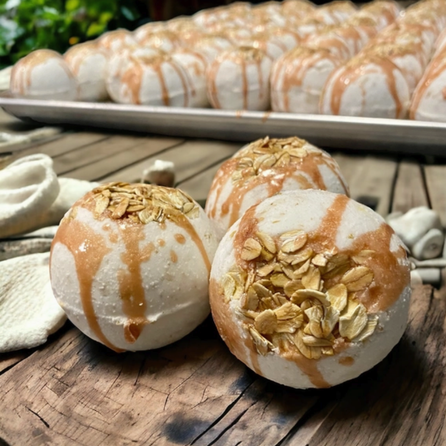 Three round white baked goods topped with caramel drizzle and oats in the foreground, with more of the same on a tray in the background on a rustic wooden surface.