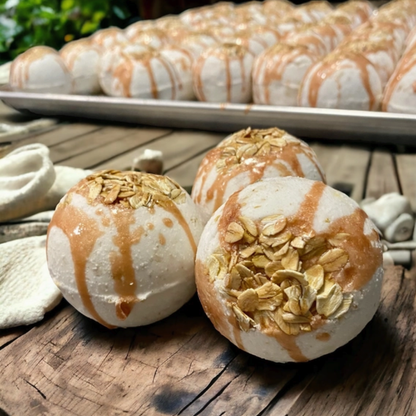 Three round white baked goods topped with caramel drizzle and oats in the foreground, with more of the same on a tray in the background on a rustic wooden surface.