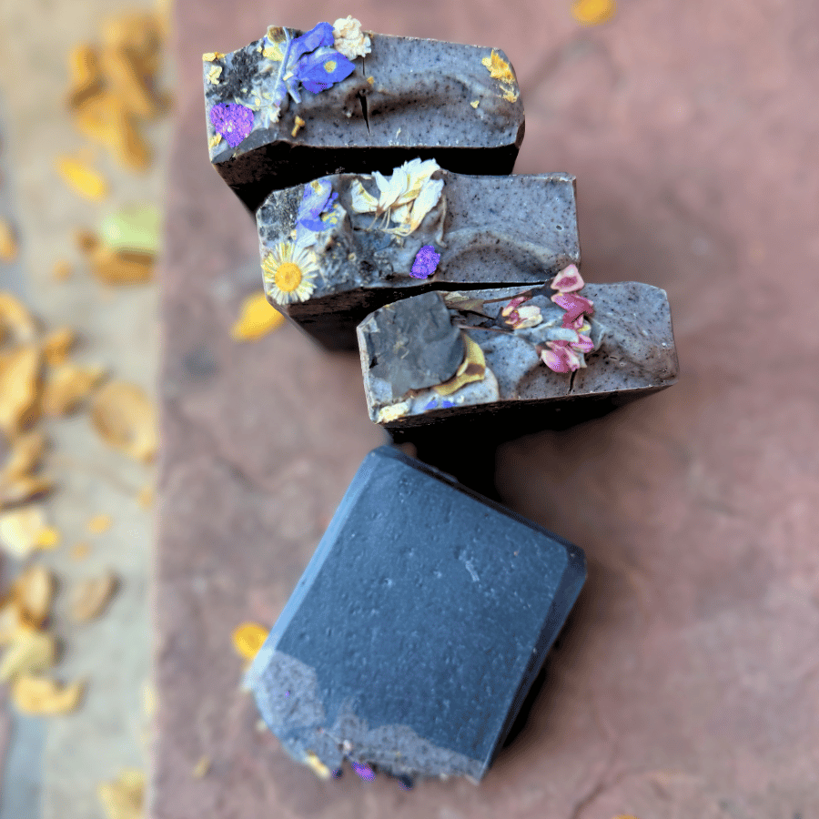 Three floral charcoal tallow soap bars arranged diagonally beside a fourth bar showing its smooth black base.