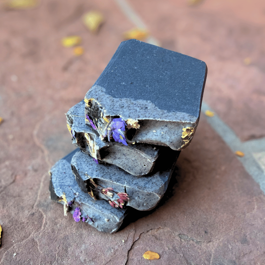 Stacked charcoal tallow soap bars showcasing deep black coloring, smoky gray marbling, and delicate pressed flowers.