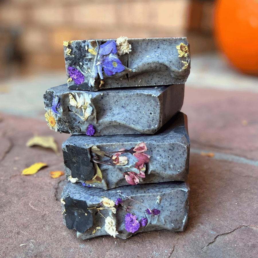 Four stacked Deep Violet charcoal tallow soap bars featuring dark gray swirls and purple, pink, and white dried wildflowers.