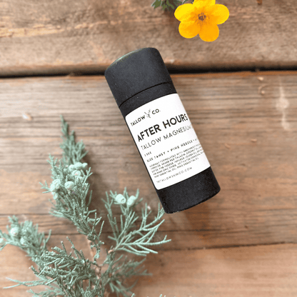 After Hours Tallow Magnesium Deodorant in a black paperboard tube, styled with yellow flowers and evergreen botanicals on rustic wood.