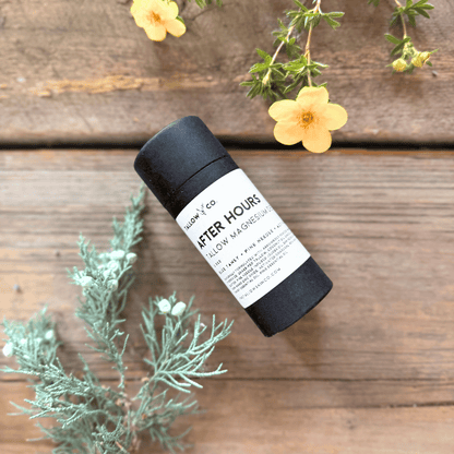 After Hours Tallow Magnesium Deodorant in black paperboard packaging, photographed with yellow blossoms and soft green botanicals on rustic wood.