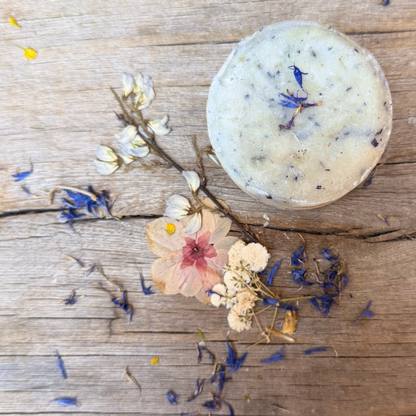 Overhead view of Butterfly Pea Facial Cleansing Bar with blue flower petals, surrounded by dried botanicals on rustic wood.