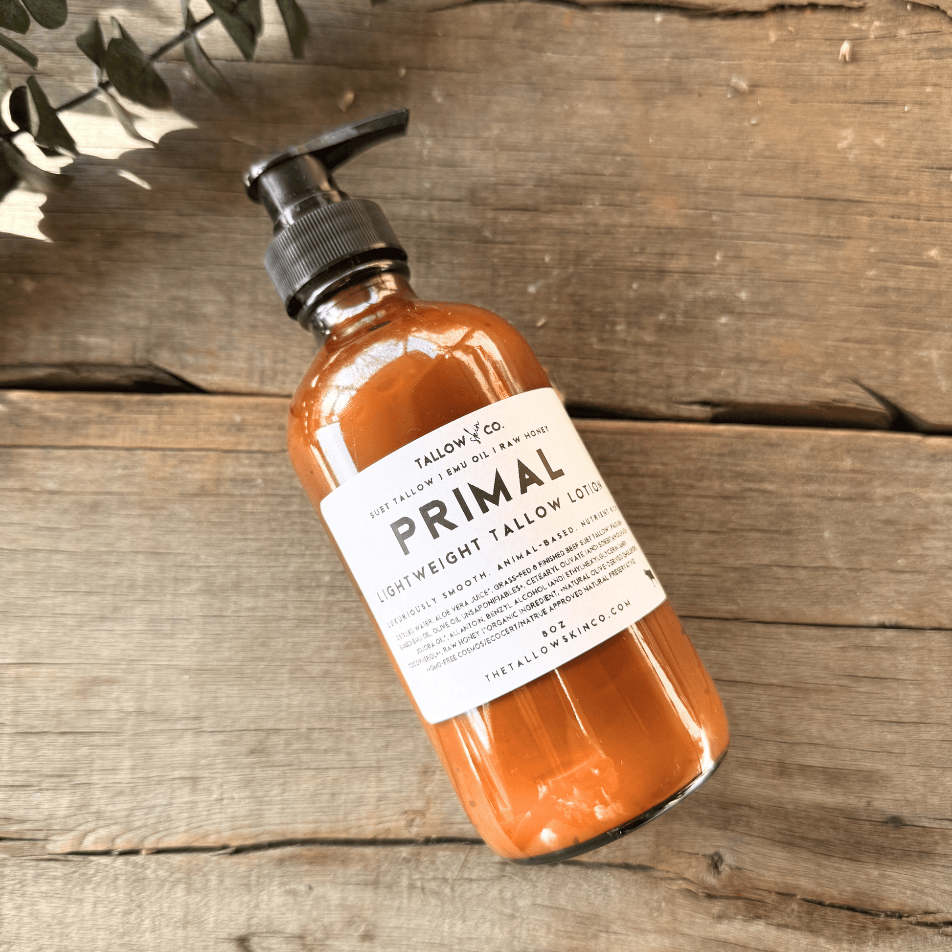 Raw honey, grass-fed suet tallow, and emu oil used in Primal natural body lotion in a glass bottle on a wooden surface. 