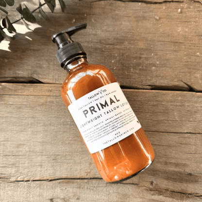 Raw honey, grass-fed suet tallow, and emu oil used in Primal natural body lotion in a glass bottle on a wooden surface. 