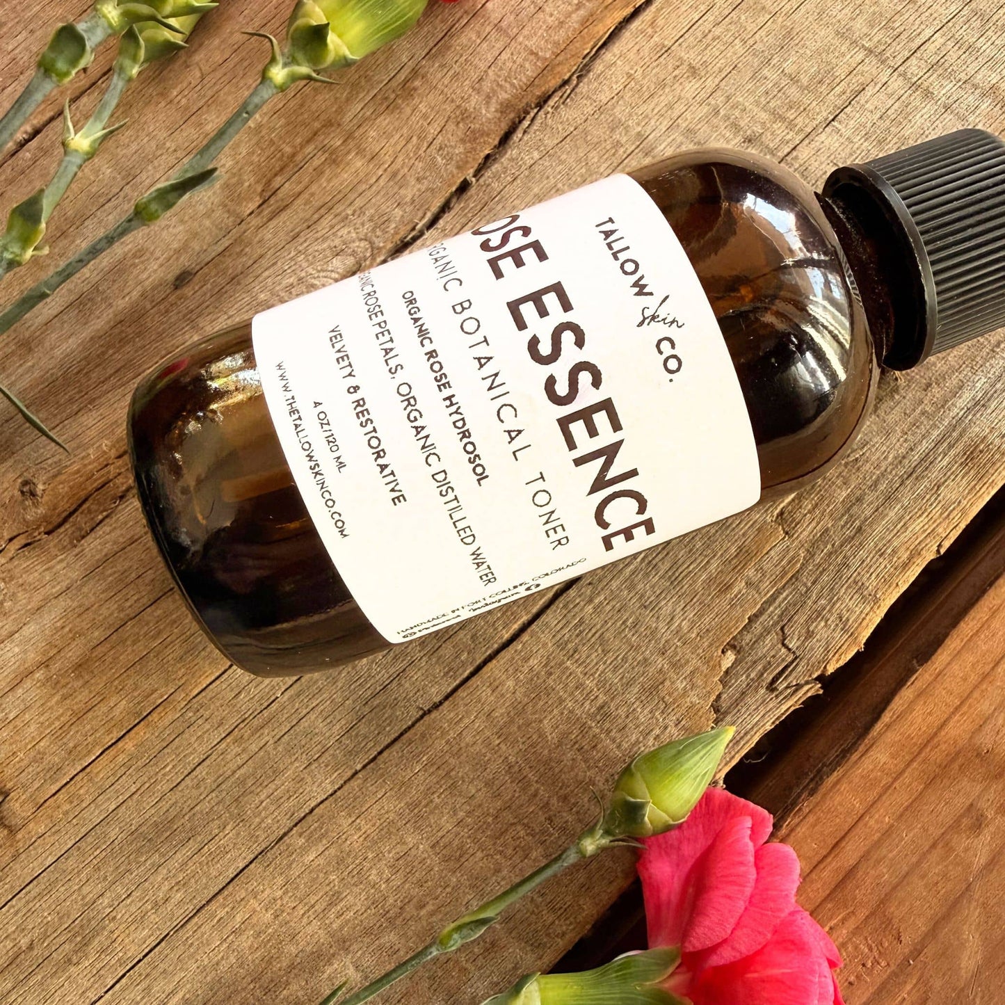 Bottle of Tallow & Co. Rose Essence Botanical Toner on a wooden surface with flowers.