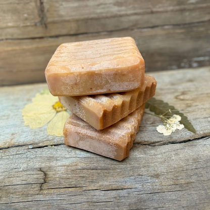 Three handcrafted Wild Blueberry Kombucha Tallow Facial Soap bars stacked on rustic wood, showcasing their golden-pink color and textured edges.