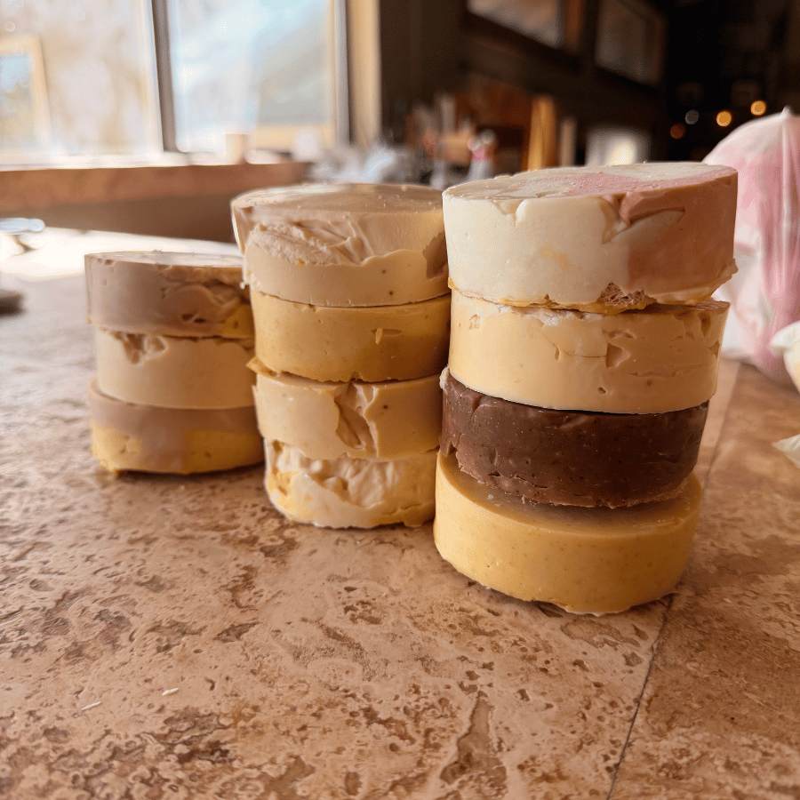 Three stacks of assorted handmade grass-fed tallow soap rounds in cream, tan, yellow, and brown, featuring rustic shapes and imperfect layers from Tallow Skin Co.'s Messies collection.