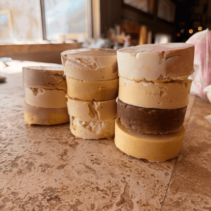 Three stacks of assorted handmade grass-fed tallow soap rounds in cream, tan, yellow, and brown, featuring rustic shapes and imperfect layers from Tallow Skin Co.'s Messies collection.