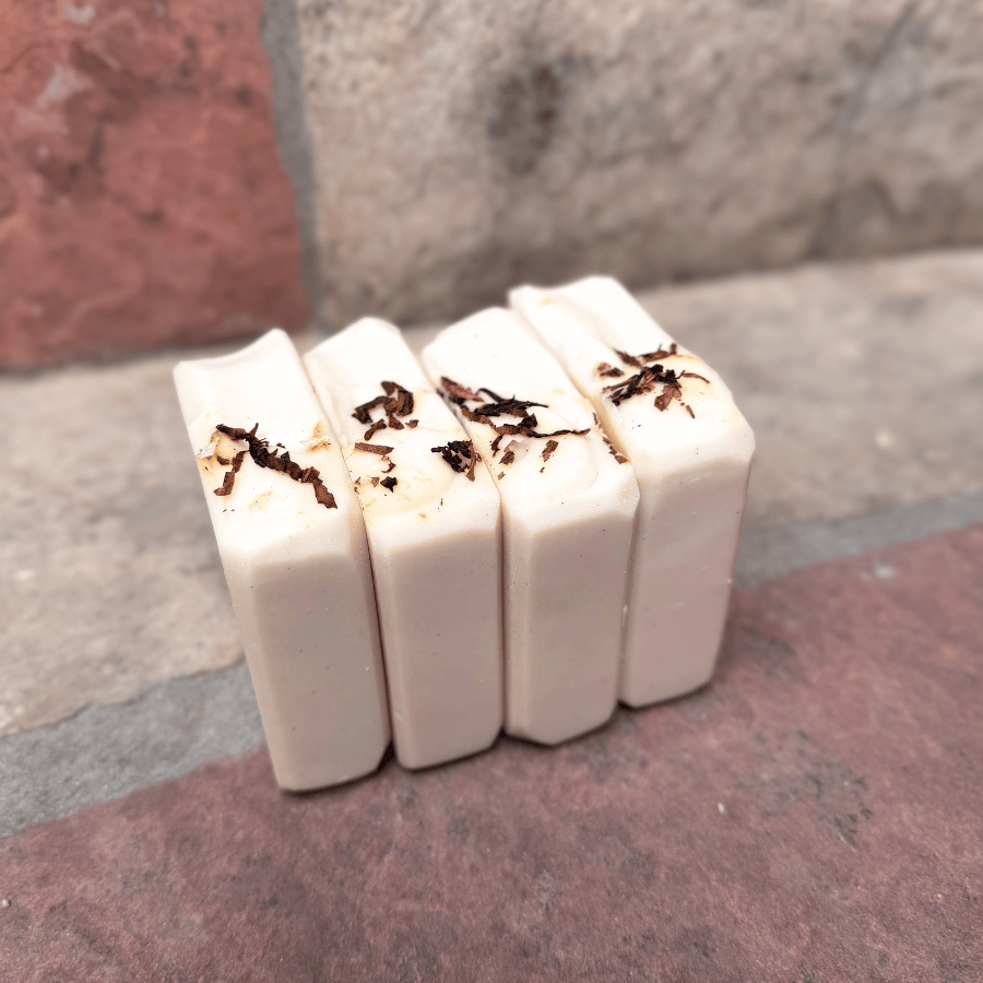 Four handmade Tobacco & Bay Leaf pumice tallow soap bars standing side by side, showing smooth ivory sides and pipe tobacco sprinkled across the tops.