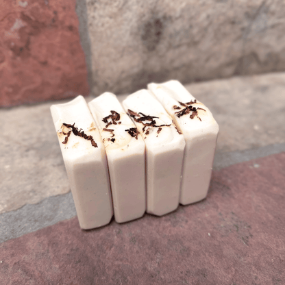 Four handmade Tobacco & Bay Leaf pumice tallow soap bars standing side by side, showing smooth ivory sides and pipe tobacco sprinkled across the tops.