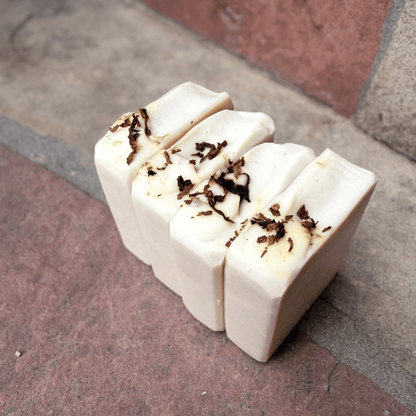 Angled view of four Tobacco & Bay Leaf exfoliating tallow soap bars featuring creamy white tops decorated with real pipe tobacco shavings.