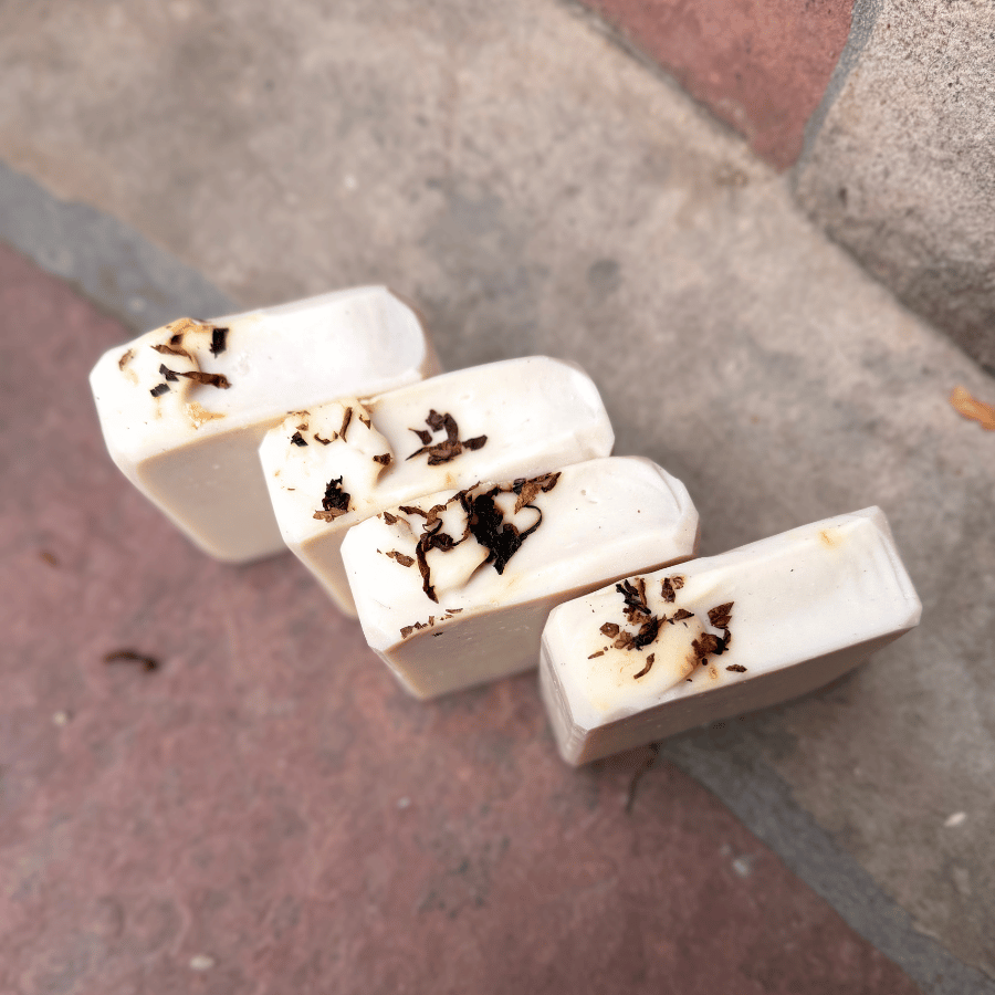 Overhead view of four handcrafted Tobacco & Bay Leaf soap bars highlighting their sculpted tops and scattered pipe tobacco accents.