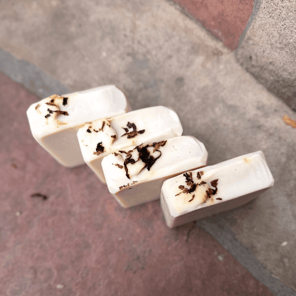 Overhead view of four handcrafted Tobacco & Bay Leaf soap bars highlighting their sculpted tops and scattered pipe tobacco accents.
